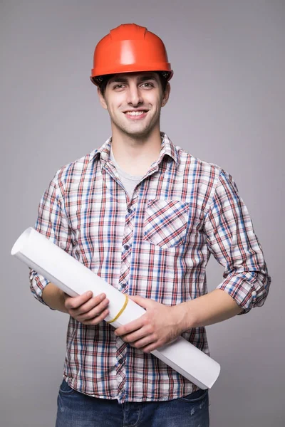 Handsome young architect in protective helmet is studying draft, on gray background — Stock Photo, Image