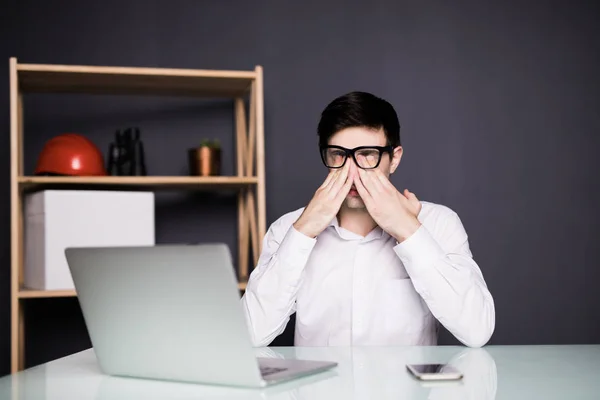 Me siento agotado. Hombre de barba joven frustrado masajeando su nariz y manteniendo los ojos cerrados mientras está sentado en su lugar de trabajo en la oficina — Foto de Stock