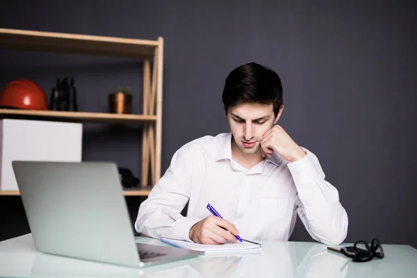 Junger Geschäftsmann reicht mit Stift Notizen auf ein Papier. Männliche Führungskraft sitzt im Büro am Tisch. — Stockfoto