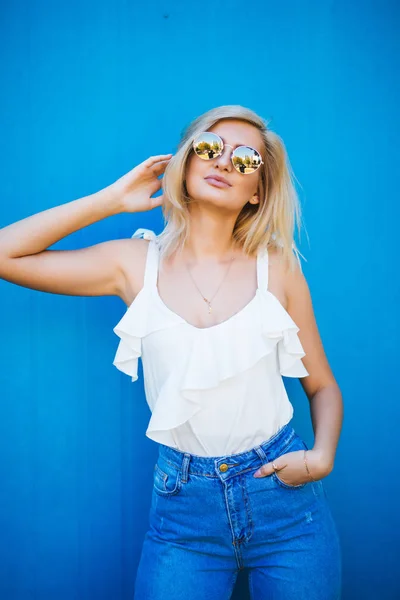 Bionda con camicia bianca e occhiali da sole su sfondo blu — Foto Stock
