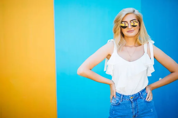 Bella giovane donna in stile biondo con contro il muro colorato . — Foto Stock