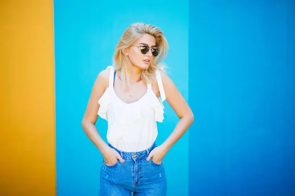Bella giovane donna in stile biondo con contro il muro colorato . — Foto Stock
