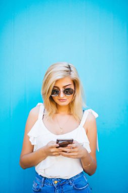 Genç güzel kadın mavi renk arka plan üzerinde cep telefonu studio kullanarak