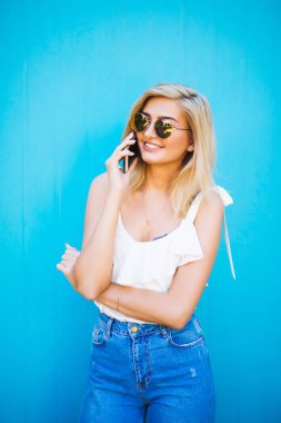 Diyen birileri cep telefonu aracılığıyla mavi duvar arka plan kopya alanı ile kameraya gülümseyen güzel kadın.