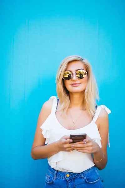 Νεαρή όμορφη γυναίκα χρησιμοποιώντας κινητό τηλέφωνο studio σε φόντο μπλε χρώμα — Φωτογραφία Αρχείου