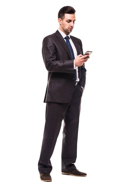 Повна довжина привабливого впевненого молодого бізнесмена в чорному костюмі з використанням мобільного телефону на білому тлі — стокове фото