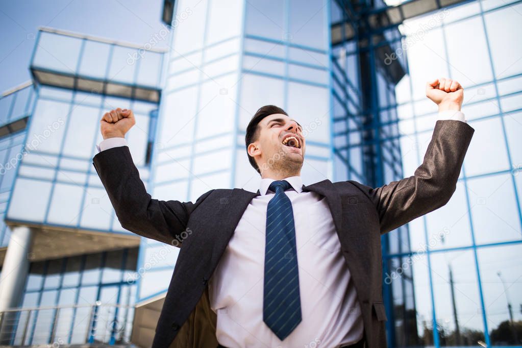 Handsome businessman raising arms in sign of victory outdoors against office building
