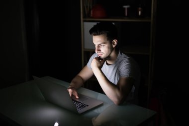 Karanlıkta bir masada dizüstü kullanarak gece geç saatlerde internet bağımlılığı veya çalışma geç adam