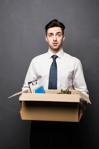 Ser despedido. Bonito homem de negócios em uso formal segurando uma caixa com suas coisas, em fundo cinza — Fotografia de Stock