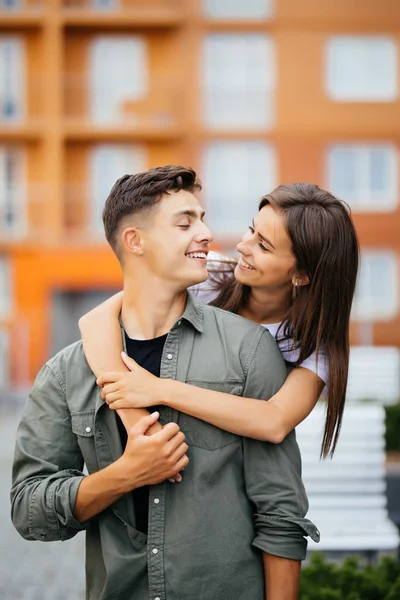 Portrait of beautiful young couple in casual clothes hugging, looking at camera and smiling in the street — Stock Photo, Image