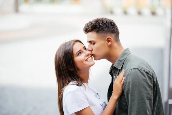 Jovem bonito beijando a bochecha de sua amada na rua — Fotografia de Stock