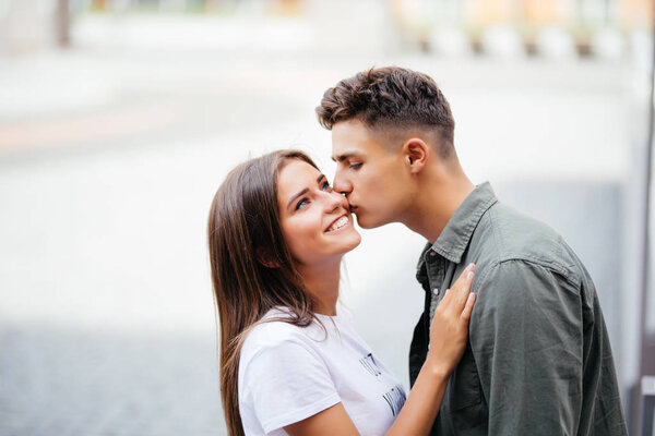 Красивый молодой человек целует свою возлюбленную щеку на улице
