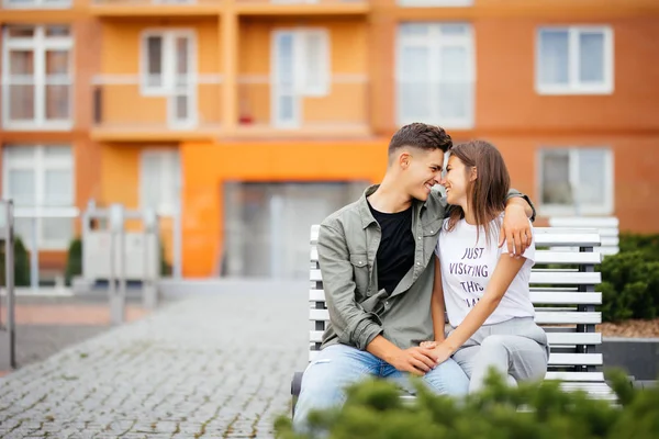 Underbara unga par i kärlek i parken på en bänk. Vacker kvinna med långt mörkt hår och en man kramas på gatan. — Stockfoto