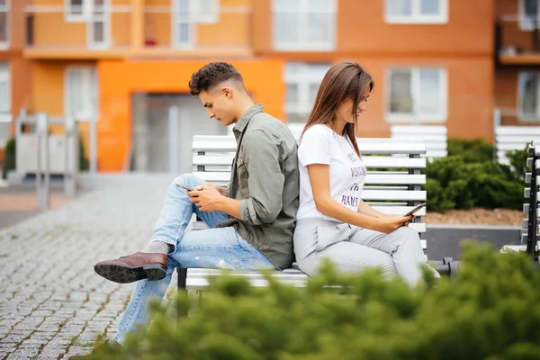 Conceito de vício em celular - casal olhando para seu telefone celular enquanto em uma data sentado no banco na rua da cidade — Fotografia de Stock