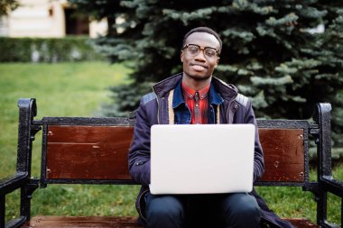 Genç Afrika neşeli adam öğrenci ve iş üstünde laptop açık havada sokakta bankta oturmuş