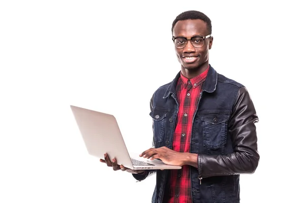 Bonito afro-americano homem está usando um laptop, olhando para a câmera e sorrindo, contra a parede branca — Fotografia de Stock