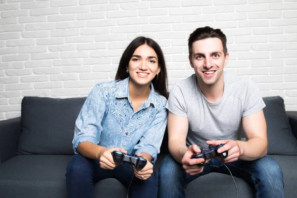 Who will win. Competition of a siblings playing car race. Excited friends are playing games indoors at home, sitting on cozy beige sofa and enjoying themselves. They have great and fun time — Stock Photo, Image