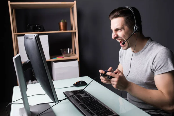 Hombre joven gritando enojado en auriculares con PC juego de ordenador en casa y streaming playthrough o video walkthrough — Foto de Stock