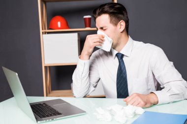 Hasta bir adam ofiste onun işyerinde oturuyor. O burnunu içine kağıt peçete uçurdu.