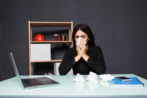 Kranke Frau sitzt an ihrem Arbeitsplatz im Büro. Eine Frau pustet sich am Arbeitsplatz die Nase zu. — Stockfoto