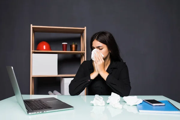 Sick woman sitting at her workplace in the office. A woman blows her nose in the workplace.