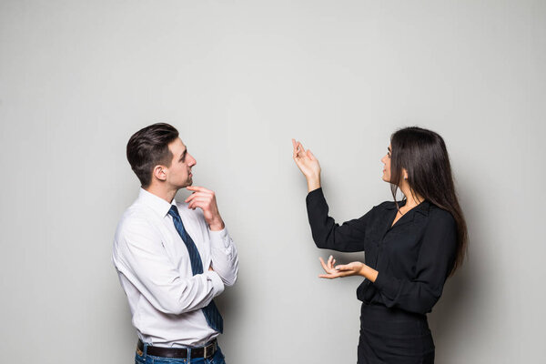 Smiling businesswoman and businessman are conversing against grey background.