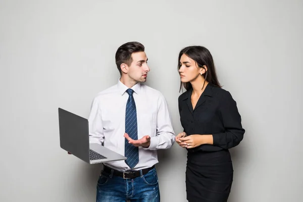 Hermosa mujer de negocios y hombre de negocios guapo en trajes formales están utilizando un ordenador portátil, hablando y sonriendo, de pie ante la pared gris — Foto de Stock