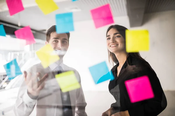 Business, startup, planning, management and people concept - happy creative team writing on stickers at office glass board — Stock Photo, Image