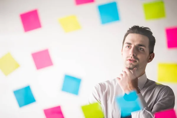 Hombre de negocios escribiendo en pegatinas en la oficina y pensando en ellos . — Foto de Stock