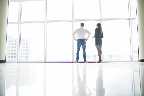 Office staff is discussing something by the window standing with their backs