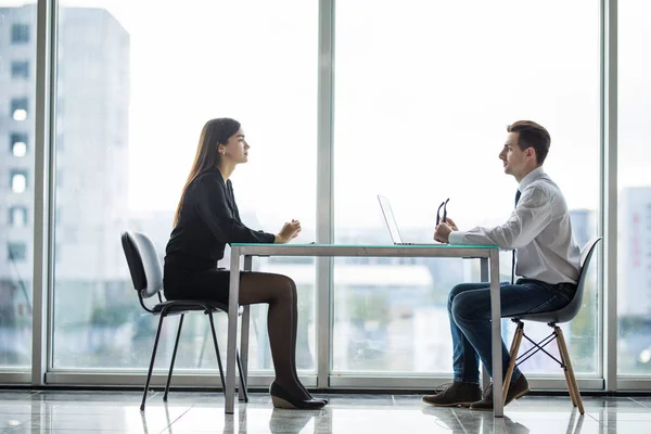 Businessman and woman having a discussion in the office face to face at table against windows