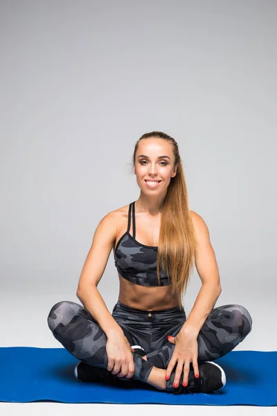 Sportif ve sağlıklı güzellik. Güzel genç kadın egzersiz mat gri arka plan üzerinde otururken gülümseme ile kameraya seyir spor giyim — Stok fotoğraf