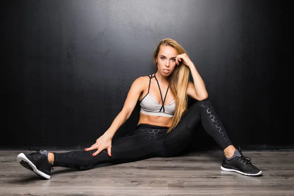 Sexiga fitness modell kvinnan sitter avslappnad på golvet på svart bakgrund — Stockfoto