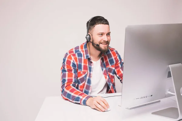 Человек, работающий за компьютером с гарнитурой в офисе за столом — стоковое фото