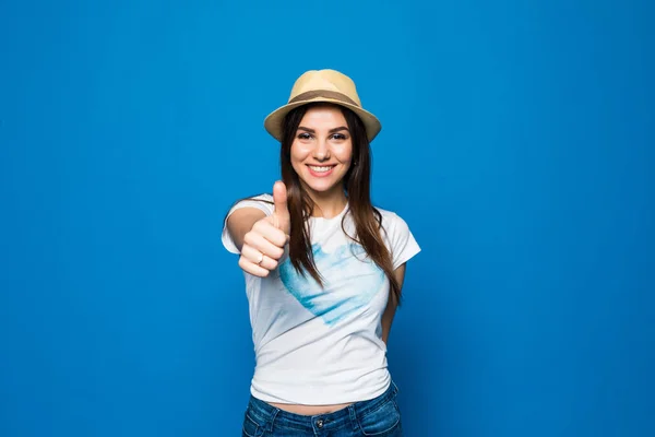 Egy mosolygó fiatal lány strand kalapot visel, és bemutatja remek gesztus mint kék elszigetelt portréja — Stock Fotó