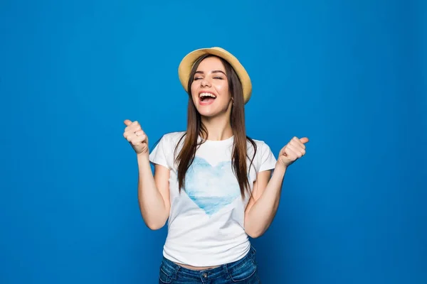 Egy boldog elégedett fiatal utazó nő a strand kalap állandó emelt kézzel festett álló alakos portréja ünnepelni győzelem a jegyek, elszigetelt, felett kék háttér — Stock Fotó