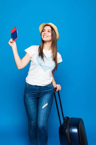 Retrato de mujer joven de moda en sombrero de mimbre de pie con maleta y pasaporte con pasaportes, sobre fondo azul — Foto de Stock