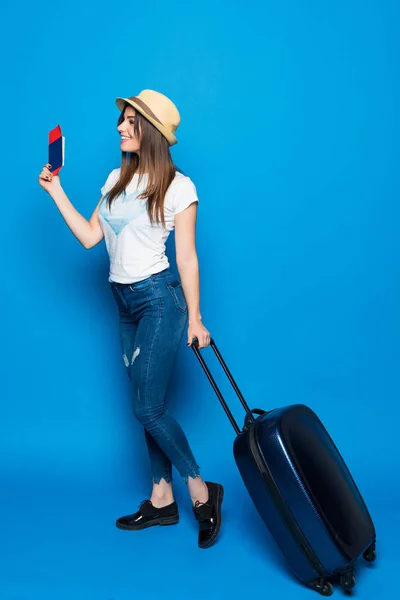 Mulher atraente nova em calça azul e um chapéu com uma mala isolada em fundo azul. Conceito de recreação e turismo . — Fotografia de Stock