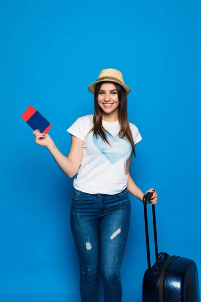 Retrato de mulher na moda jovem em chapéu de vime de pé com mala e segurando passaporte com bilhetes, sobre fundo azul — Fotografia de Stock