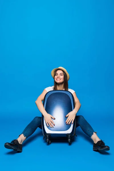Jeune femme assise près d'une valise bagages sur un fond bleu . — Photo