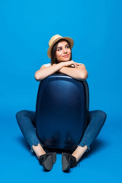 青色の背景にスーツケースの荷物のそばに座って若い女性. — ストック写真
