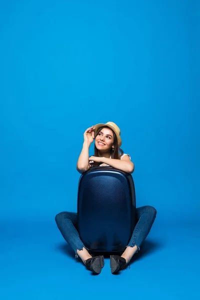 A fiatal szépség nő ült a padlón, a kék háttér utazási poggyásszal — Stock Fotó
