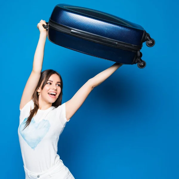 Молода красуня з піднятим багажем над головою схвильована емоціями щаслива і готова до подорожей на синьому фоні . — стокове фото