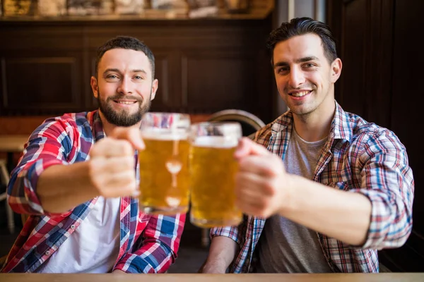 A beber uma cerveja com um amigo. Dois jovens alegres brindam com cerveja enquanto se sentam juntos no bar — Fotografia de Stock