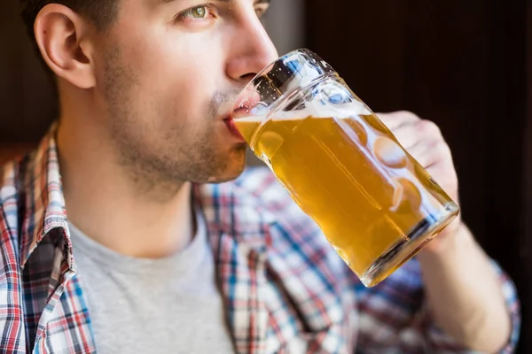 Um homem a beber cerveja. Vista lateral de belo jovem bebendo cerveja enquanto estava sentado no pub — Fotografia de Stock