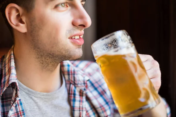 Um homem a beber cerveja. Vista lateral de belo jovem bebendo cerveja enquanto estava sentado no pub — Fotografia de Stock