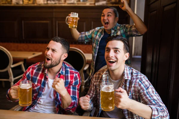happy football fans or male friends drinking beer and celebrating victory at bar or pub