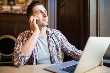 Zevk ile çalışma. Üstten Görünüm mutlu genç adam cep telefonda konuşurken ve diz üstü masa başında otururken arıyorsunuz