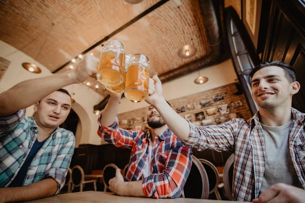 Reunión de viejos amigos. Primer plano de tres jóvenes felices en ropa casual tostadas con cerveza mientras están sentados en un pub de cerveza juntos —  Fotos de Stock