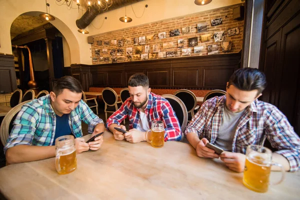Amigos do sexo masculino com smartphones viciados beber cerveja no bar ou pub — Fotografia de Stock